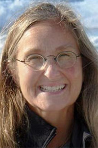 Smiling woman with round glasses and long brown hair streaked with gray