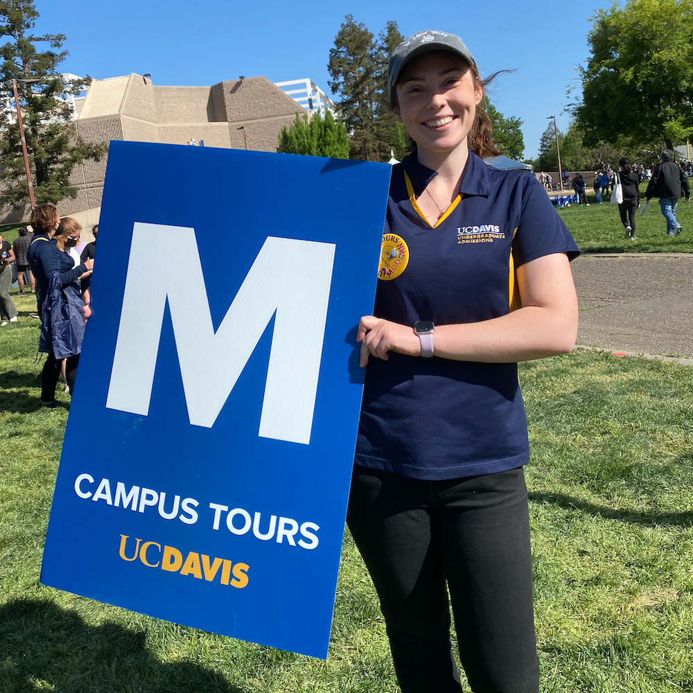 A student holds up a campus tour sign outside at UC Davis.
