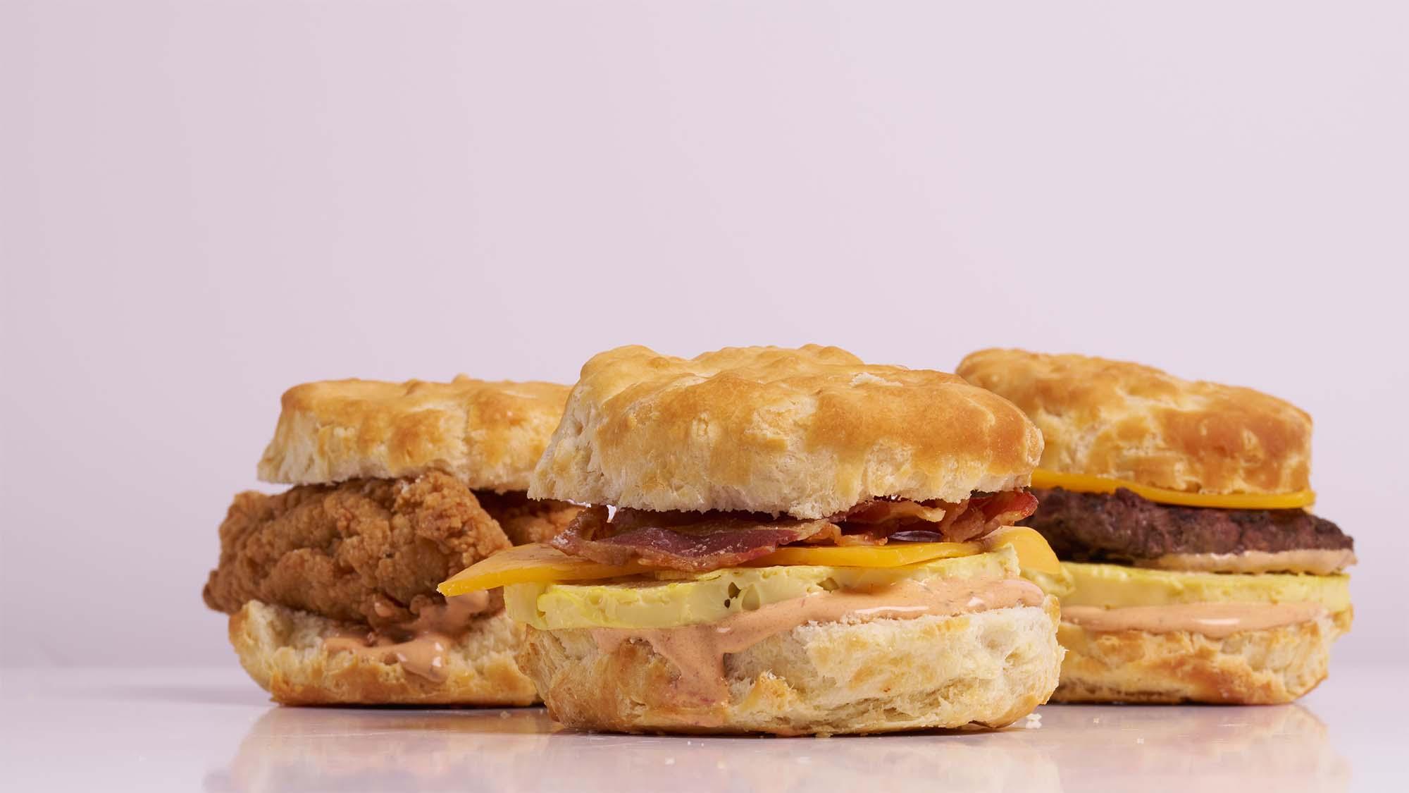 Three biscuit breakfast sandwiches with egg, cheese, fried chicken and sausage on pink