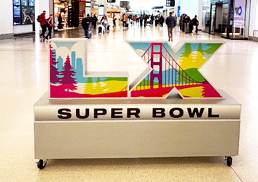 Colorful LAX Super Bowl sign with iconic bridge design in a busy airport terminal.