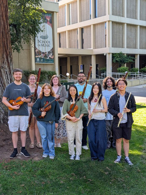 music students at workshop post on campus outdoors on green grass with building behind them