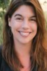 Smiling woman with long brown hair in a natural outdoor setting.