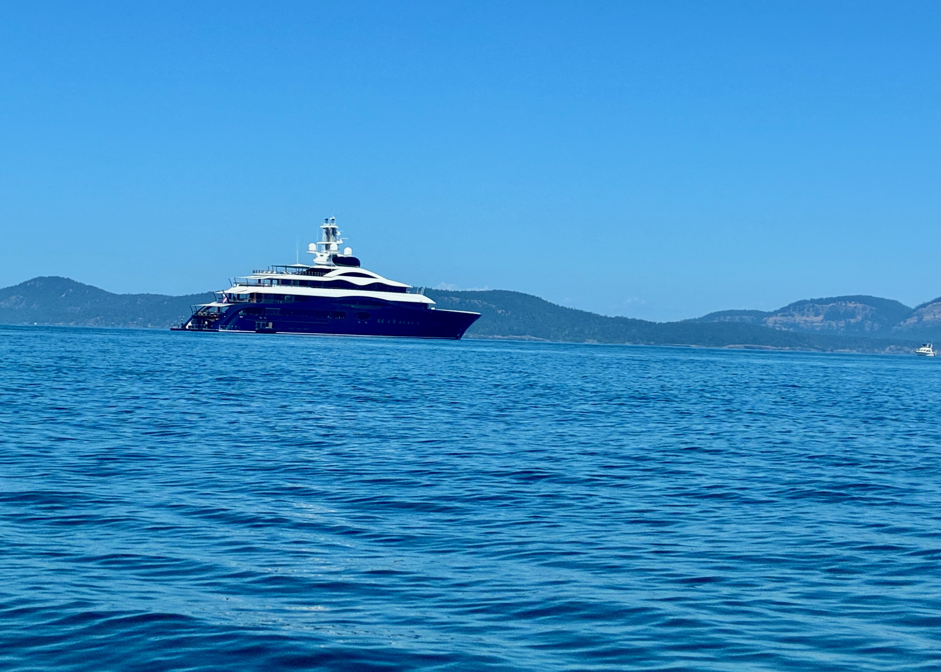 Luxury yacht on calm blue sea with distant island hills under clear sky