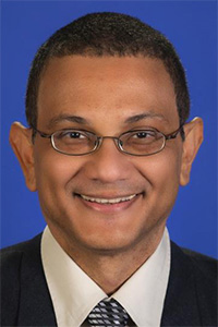 Smiling man in a suit with glasses, set against a blue background.