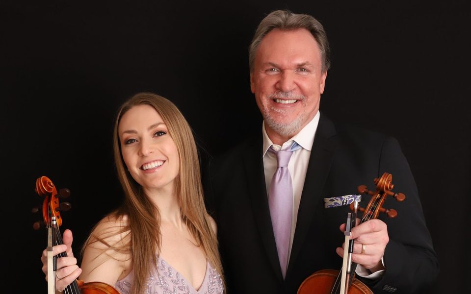 A man and woman, holding instruments, pictured on stage