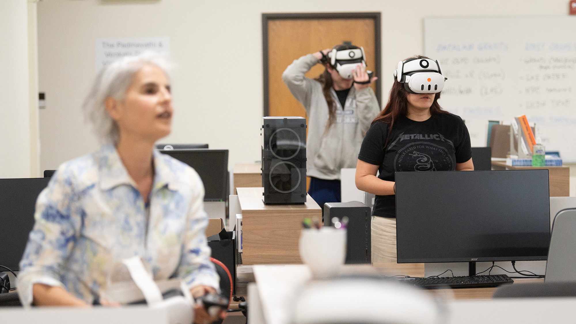 Classroom scene with two people wearing VR headsets at desks, instructor in foreground.