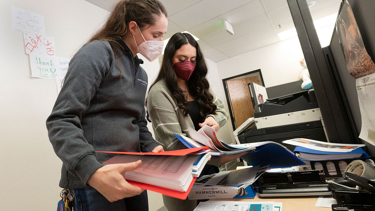 Two women review material in three-ring binders