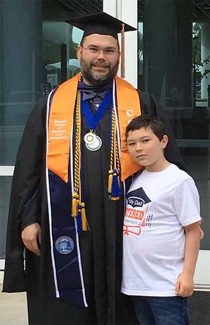 Dan Ransom in commencement regalia poses with son