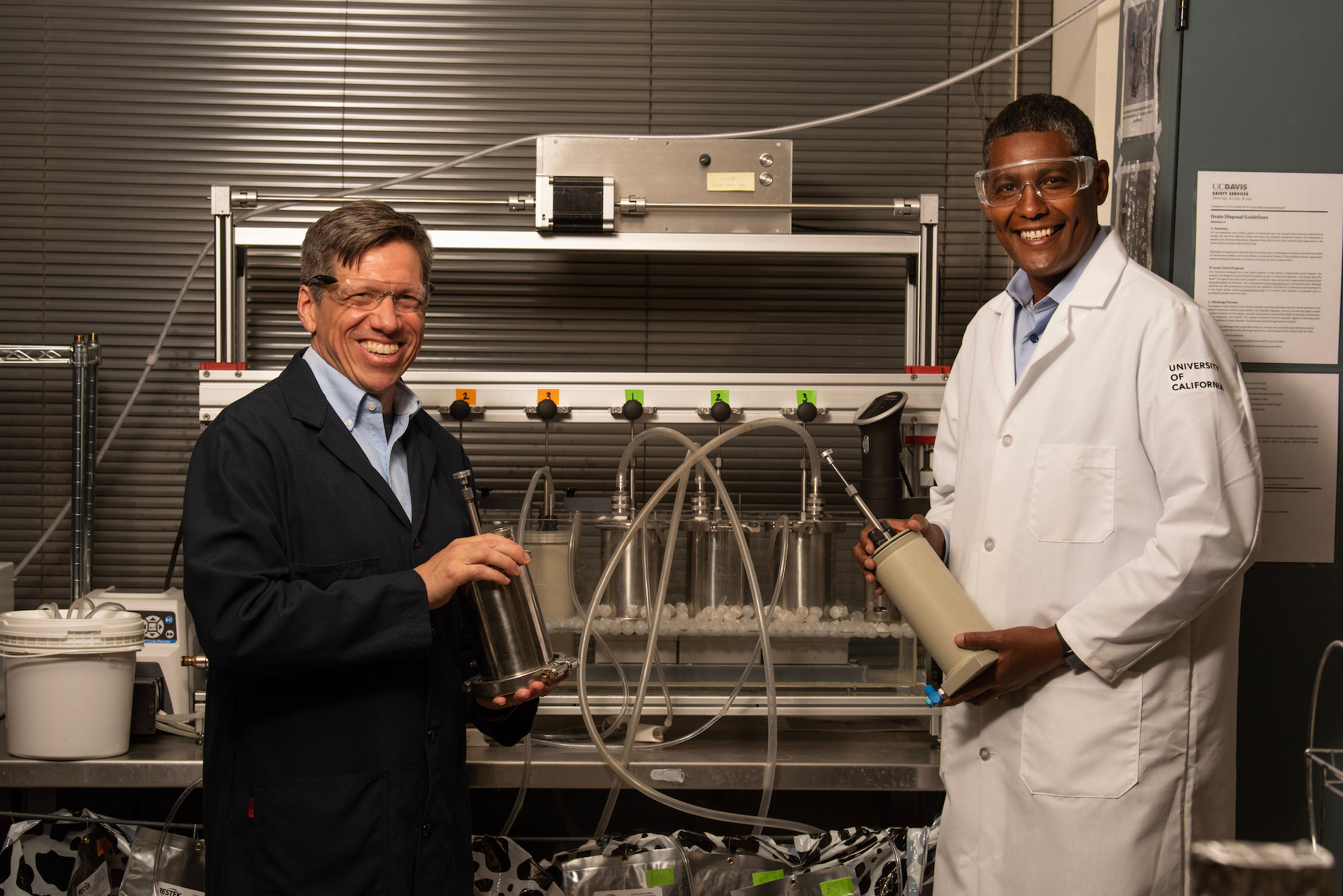 Matthias Hess, left, and Ermias Kebreab, right, stand in front of an artificial cow gut system in Hess's lab where he studies microbes. (Gregory Urquiaga/UC Davis)