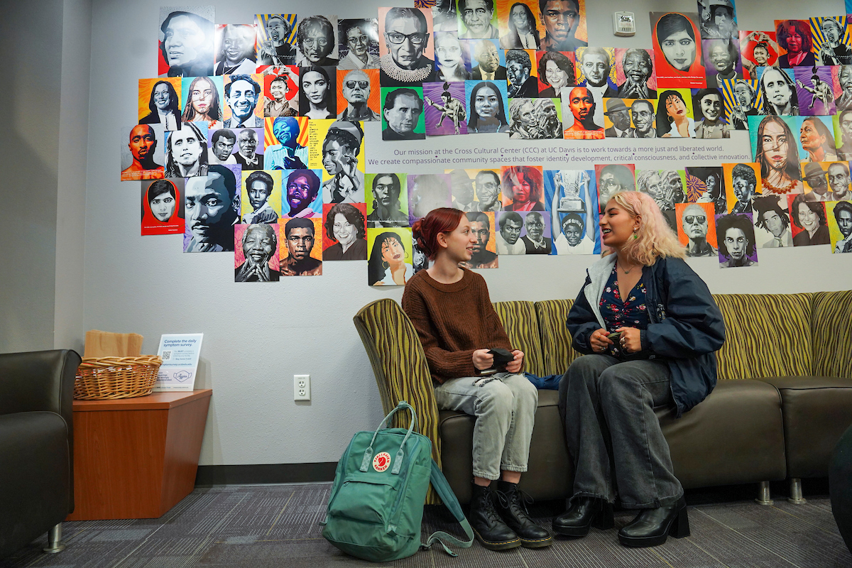 Two students chat on a couch in front of a bright mural at UC Davis.