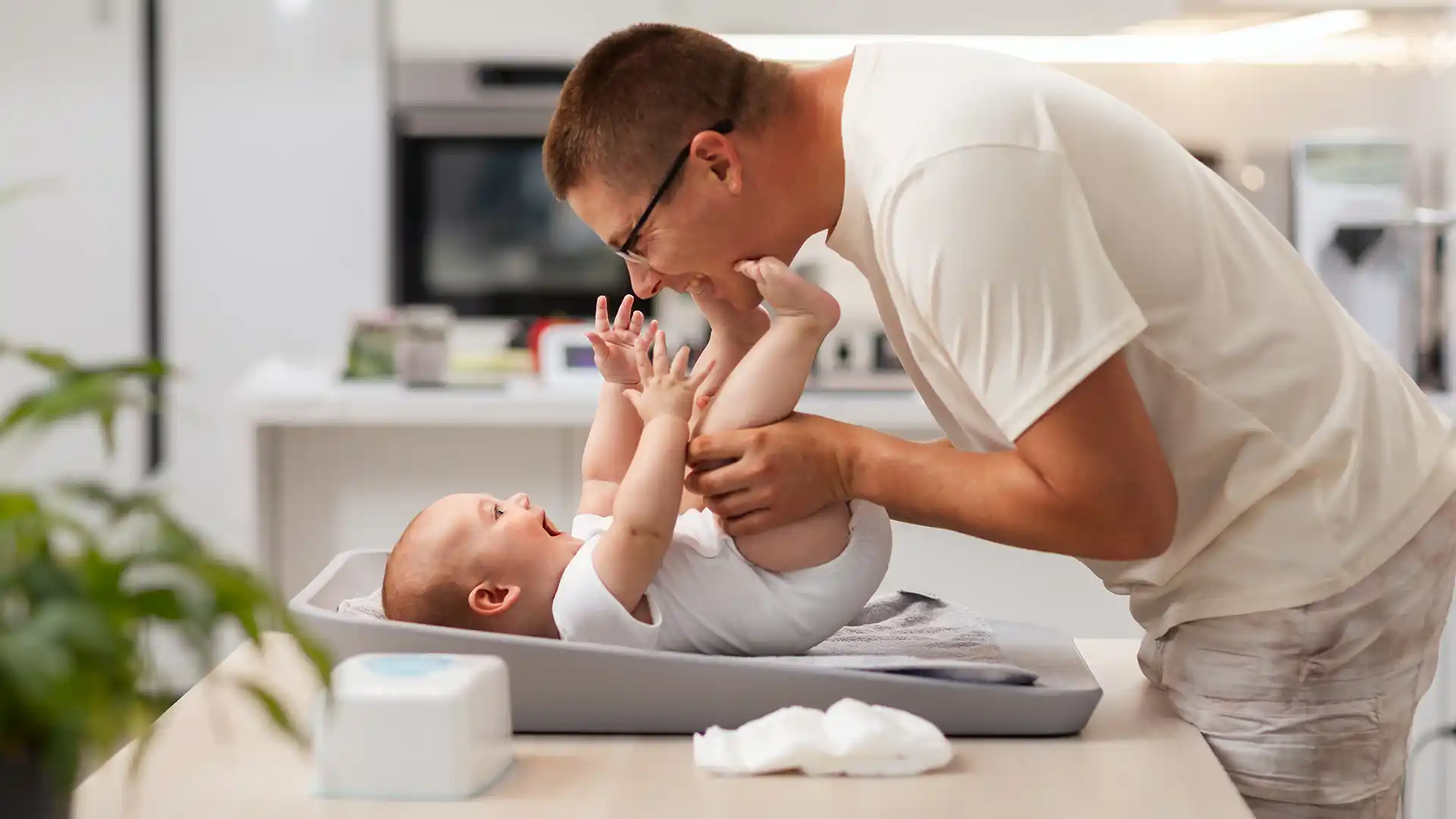 A man leans over to play with his baby before changing a diaper.