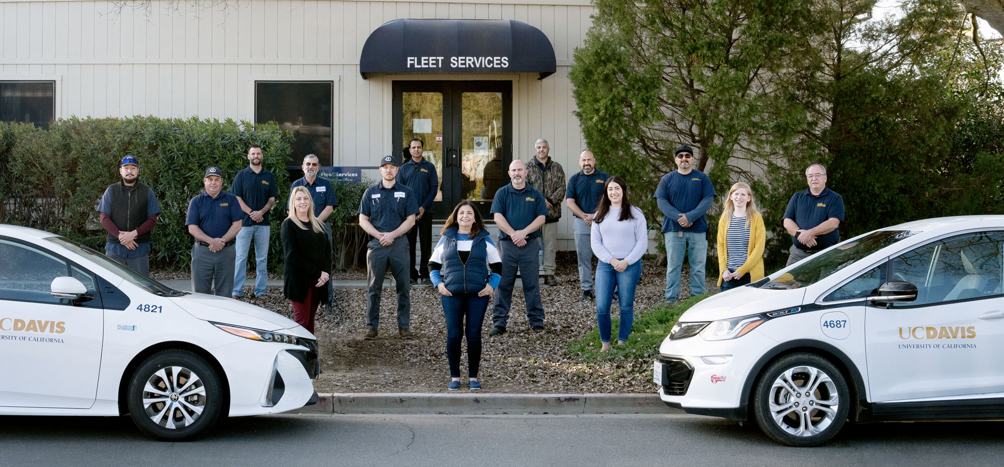 Fleet Services crew, 6-feet distanced, posing, behind two UC Davis cars