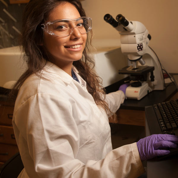 A females student smiles next to a telescope