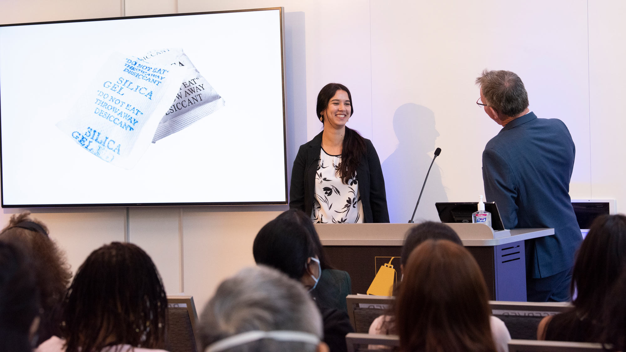 Female Grad Slam contestant, after her presentation, chats with man at podium,
