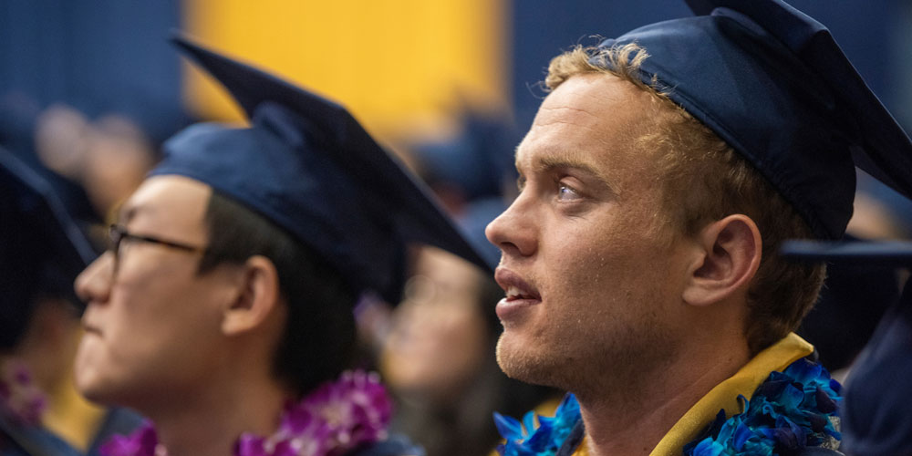 Two students prepare to graduate while listening to the commencement speaker address the audience