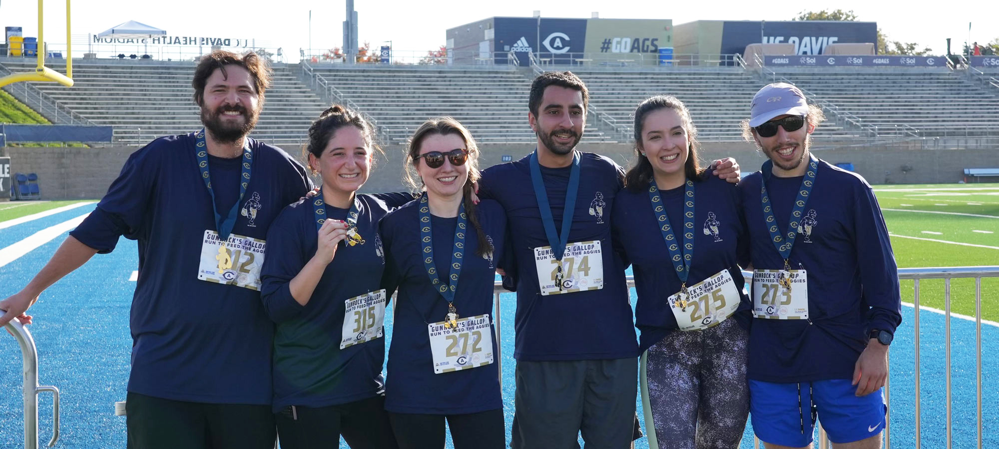 Six Gunrock's Gallop participants, posing in a line, all in blue shirts and wearing medals