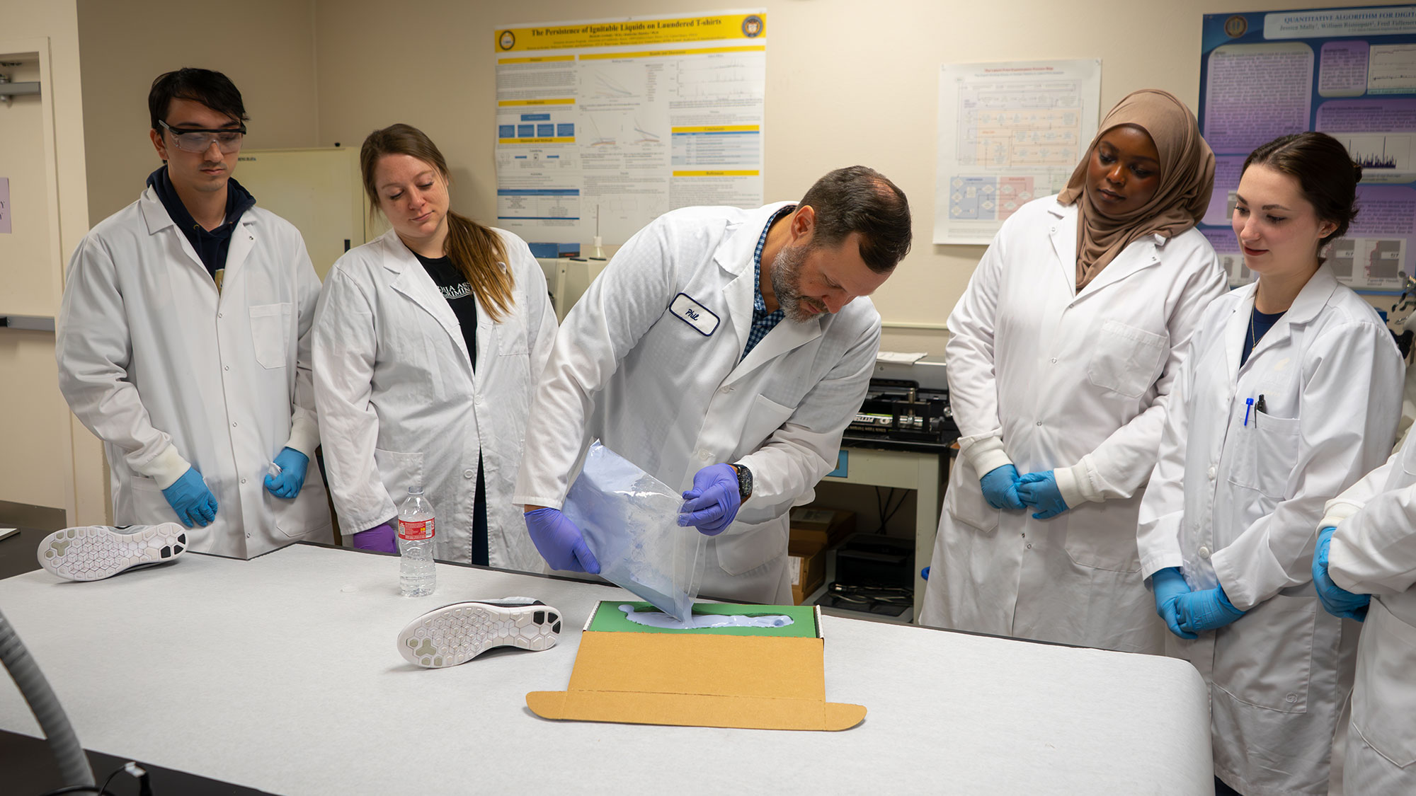 Students watch their teacher prepare a footprint sampling on a lab bench