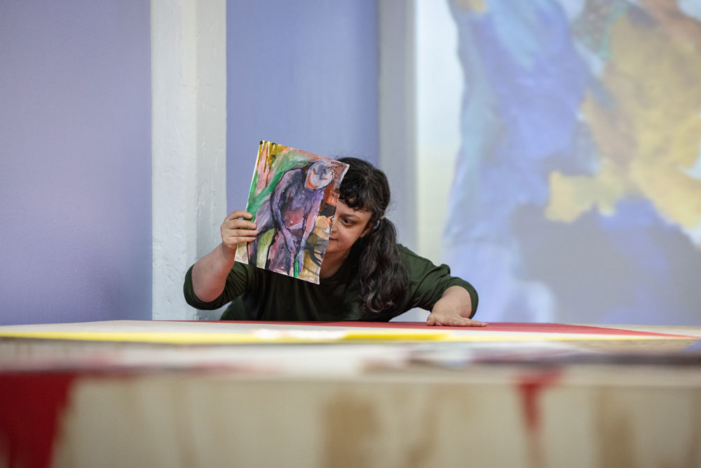 Artist holdiing painting while standing over table 