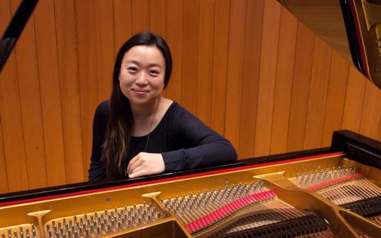 Woman with long dark hair and dark clothing sitting at piano