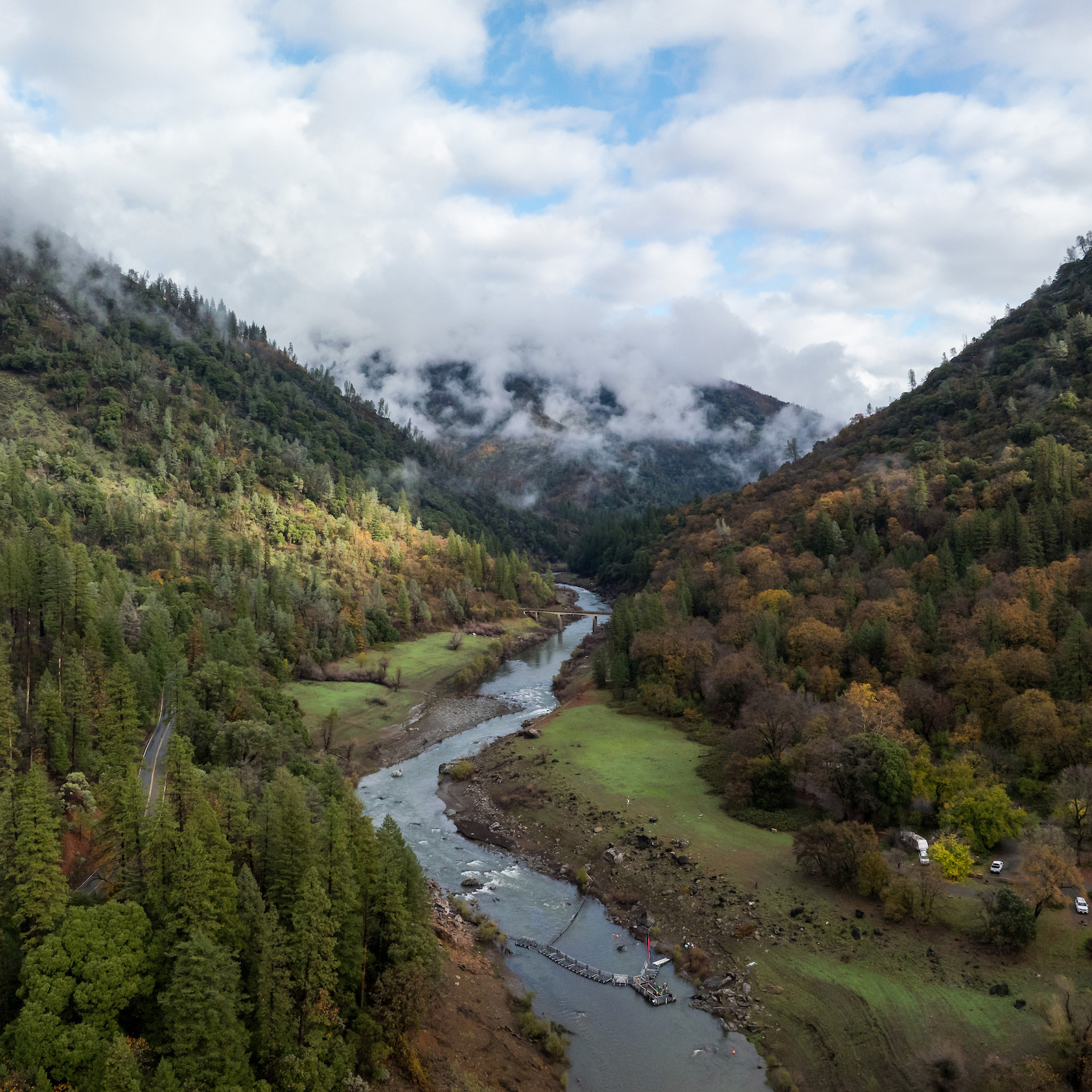 Aerial view of winding river through forested valley, misty hills and cloudy sky