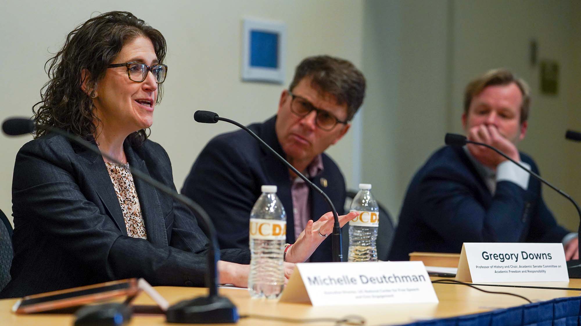 Woman speaks into microphone while two men look on.