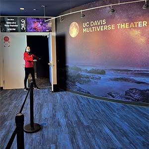 Woman makes welcoming gesture near door to UC Davis Multiverse Theater