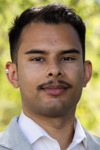 Headshot portrait of a man with mustache in light gray suit against blurred green background
