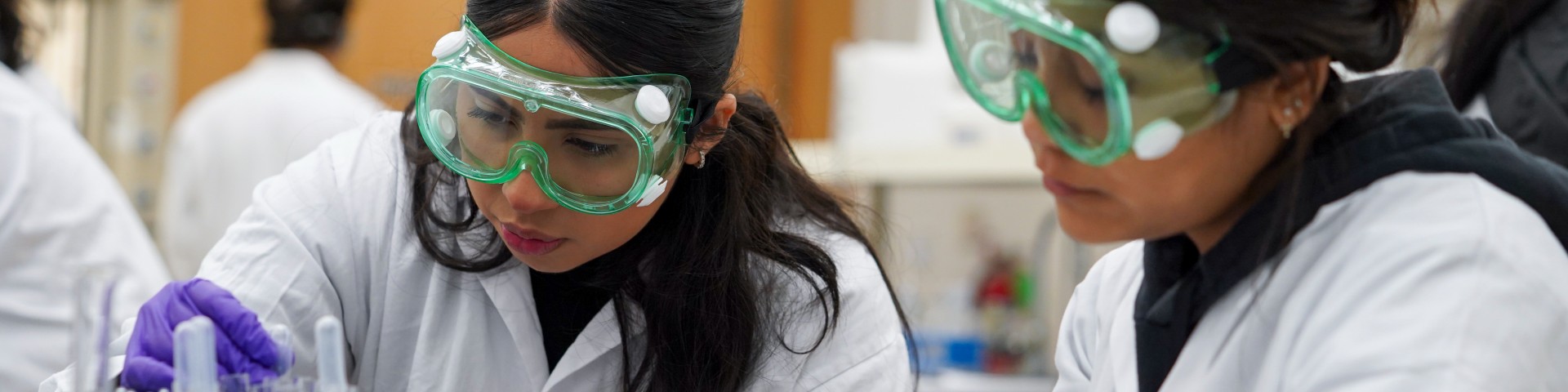 two chemistry tudent wear goggles at a lab bench while dealing with pharmaceuticals at UC Davis