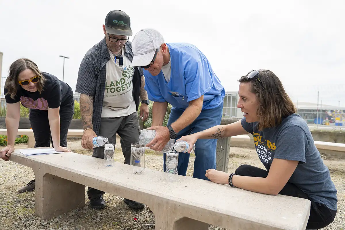 Four people pouring water through soil and filters into plastic bottles