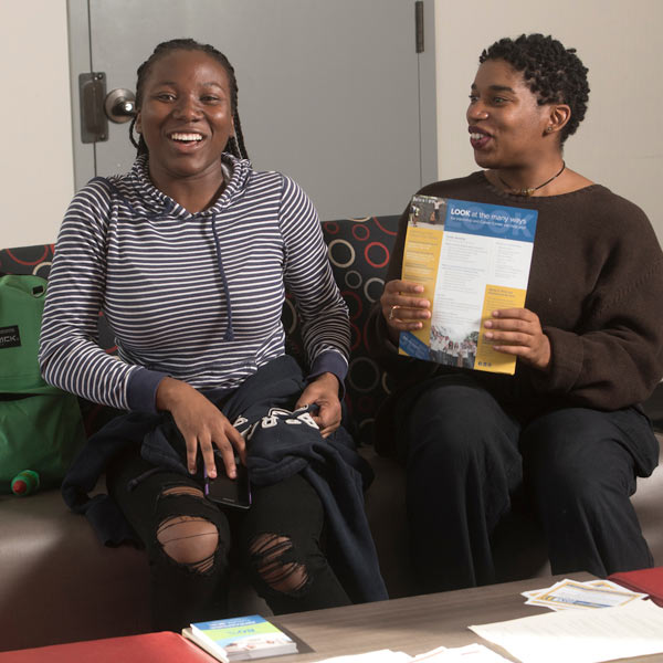 two females students laugh while studying on a couch