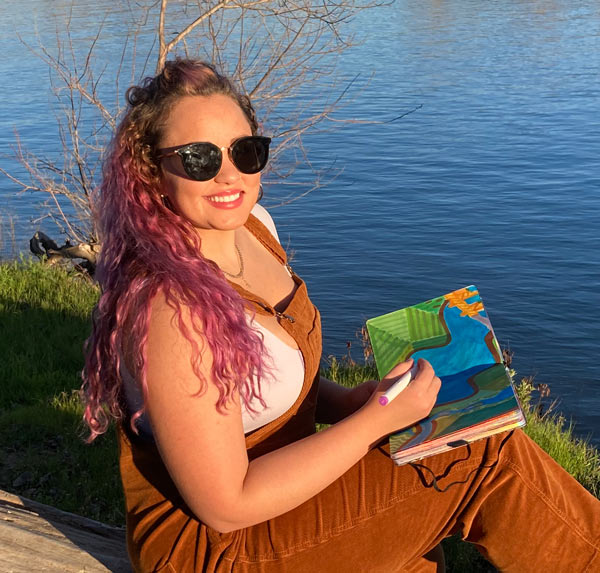 Woman sits along river, painting