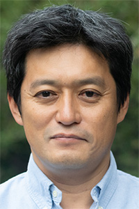 Man in a portrait photograph, short dark hair, neutral expression, light blue shirt