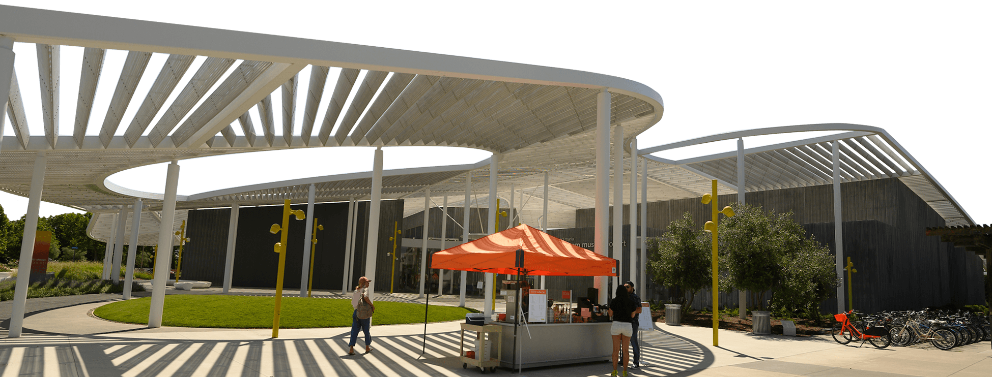 Modern outdoor plaza with white circular canopy, striped paving, and orange-umbrella food cart