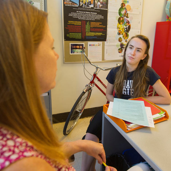 A female student attends office hours with her professor with a bicycle in the background