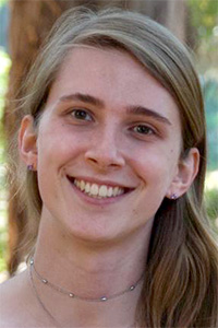 Smiling woman with long light-brown hair and delicate necklace outdoors