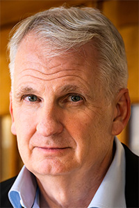 Close-up portrait of man with gray hair, neutral expression, warm indoor background