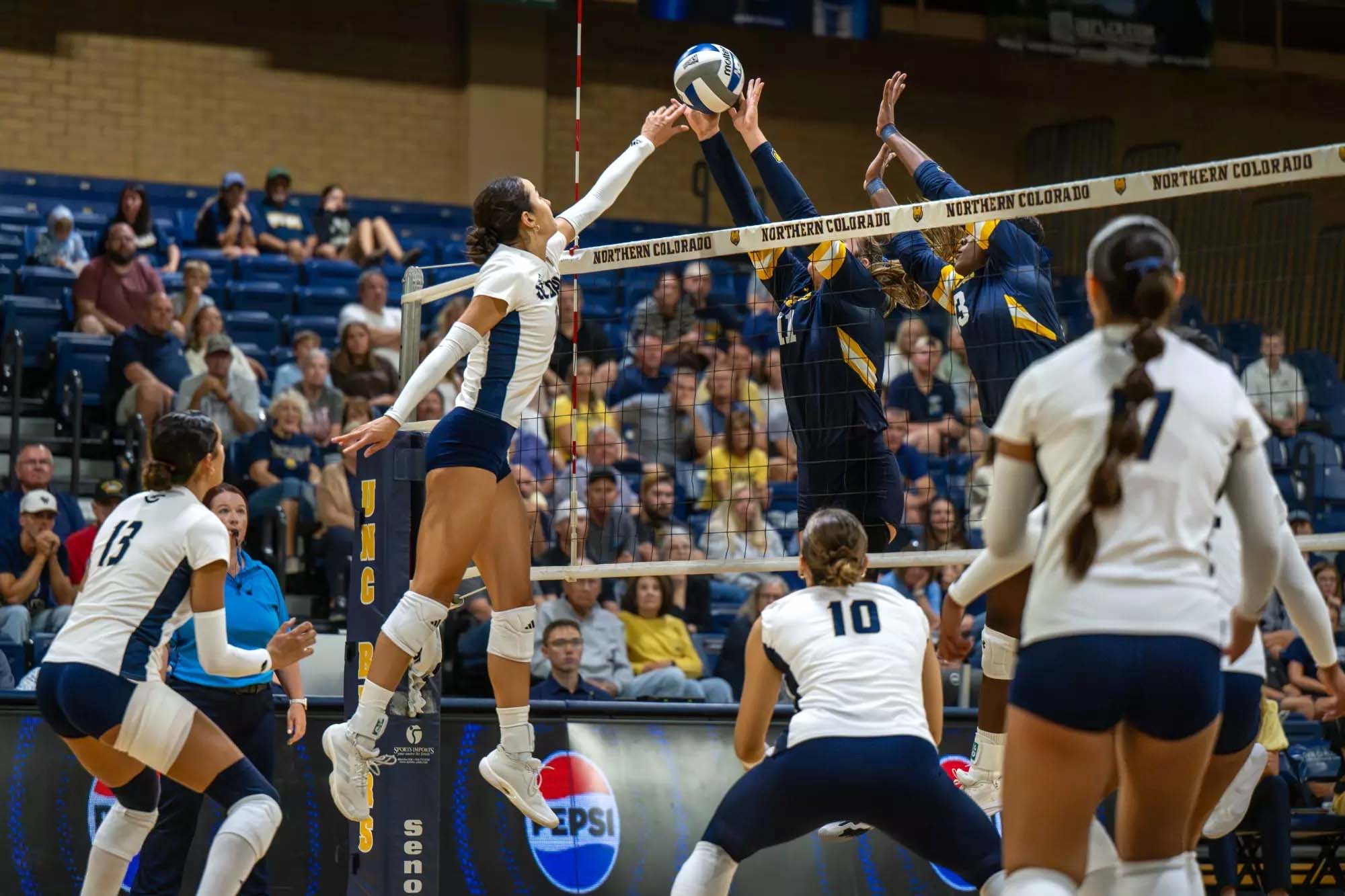 Women's volleyball action: attacker spiking as opponent blocks at net, crowd in stands