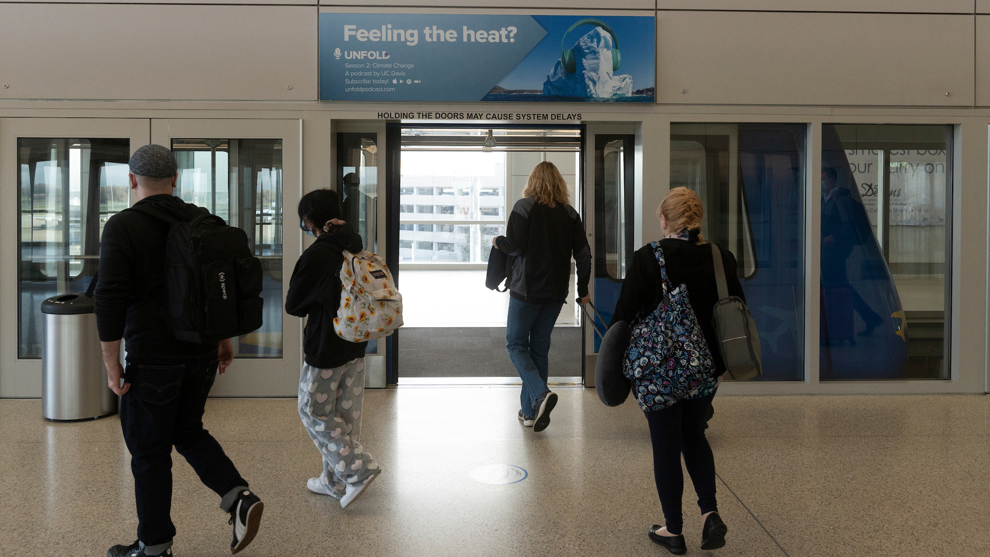 People walk under "Unfold" advertisement at airport.