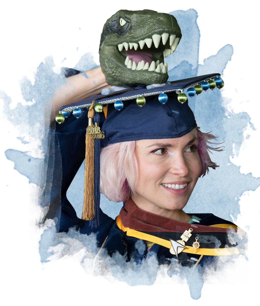 A student dressed for graduation with a t-rex head atop her grad cap