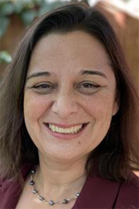 Smiling headshot of woman, shoulder-length dark hair, maroon jacket, wearing necklace