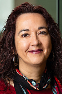 A woman with wavy brown hair, smiling, wearing a red top and a colorful scarf.