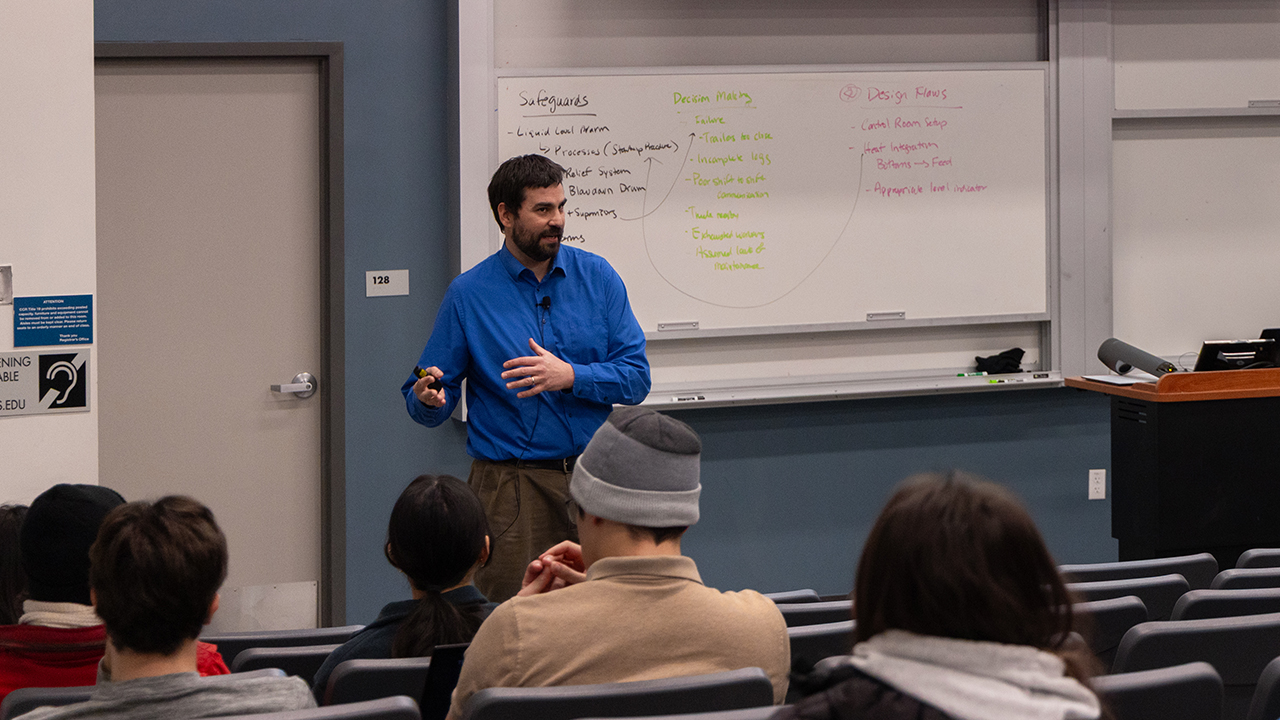 Instructor in blue sweater speaking to seated students in classroom