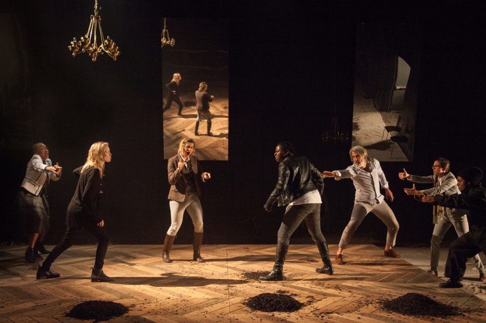 Darkened theater with performers on stage illustrating Mondavi play.