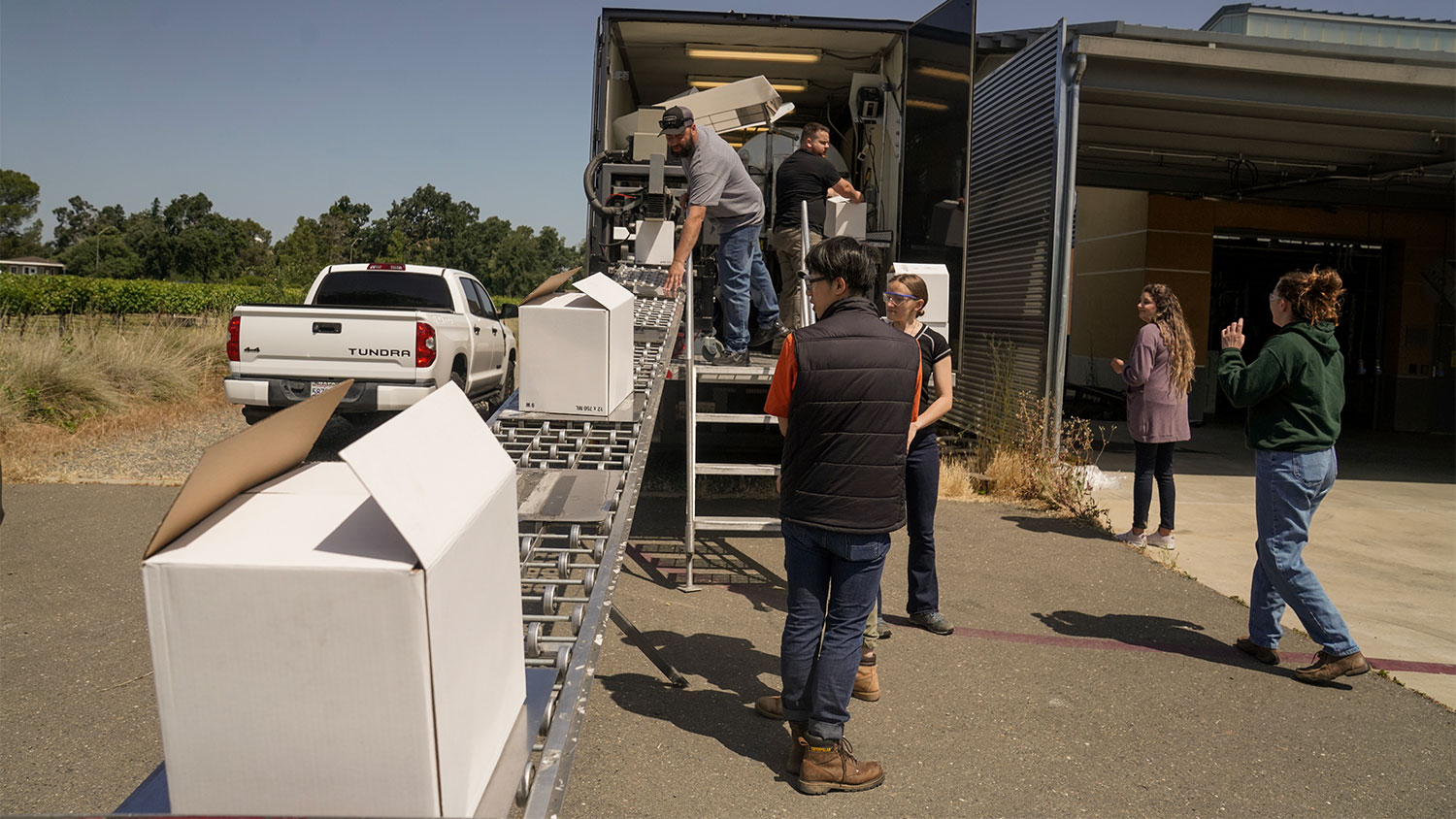 A Halsey Bottling employee places the boxed wine onto a conveyor belt to exit the mobile bottling trailer while VEN127L students watch. (Karin Higgins/UC Davis)