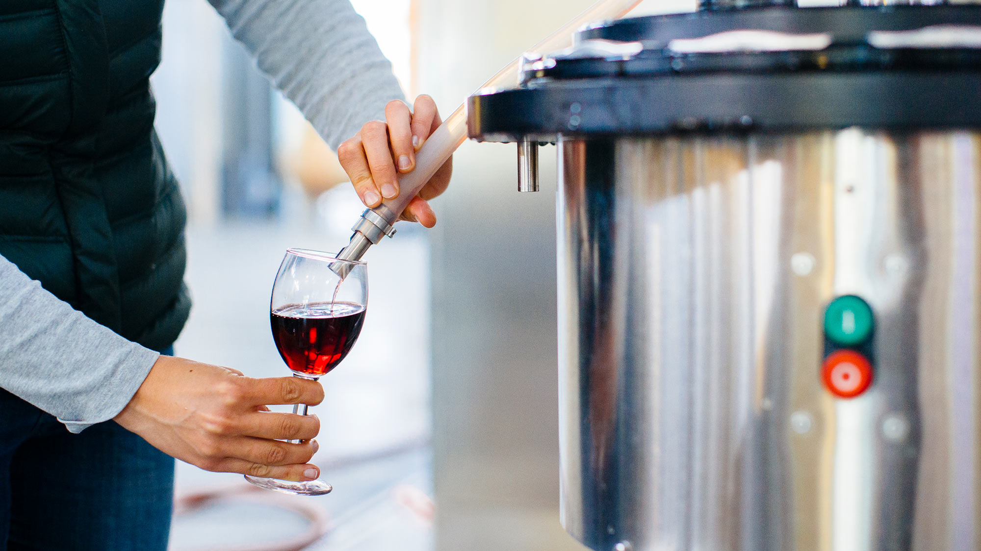 Faceless hand draws a sample of wine from a tank