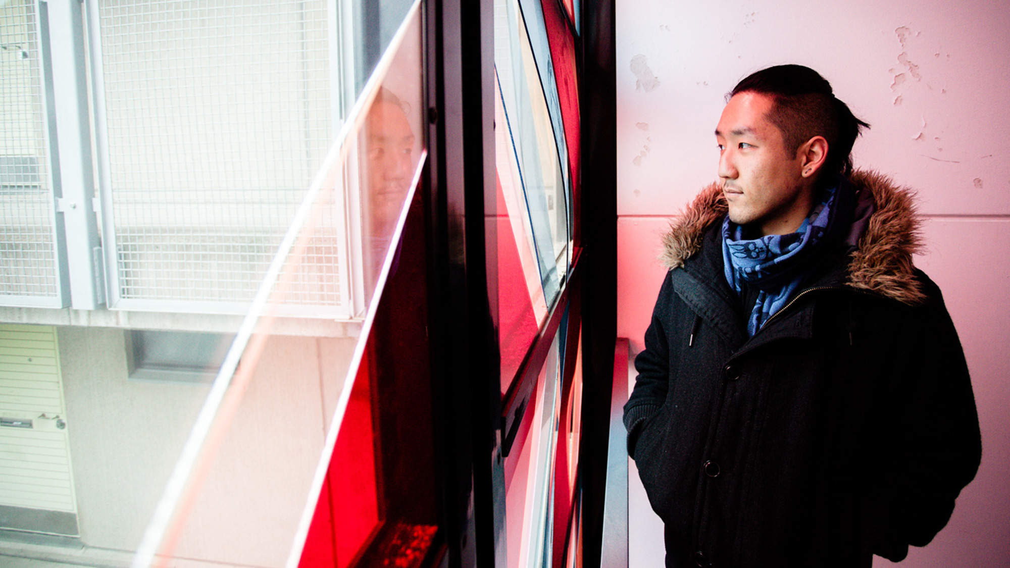 Man in black coat and blue scarf gazes through red-tinted window, photograph