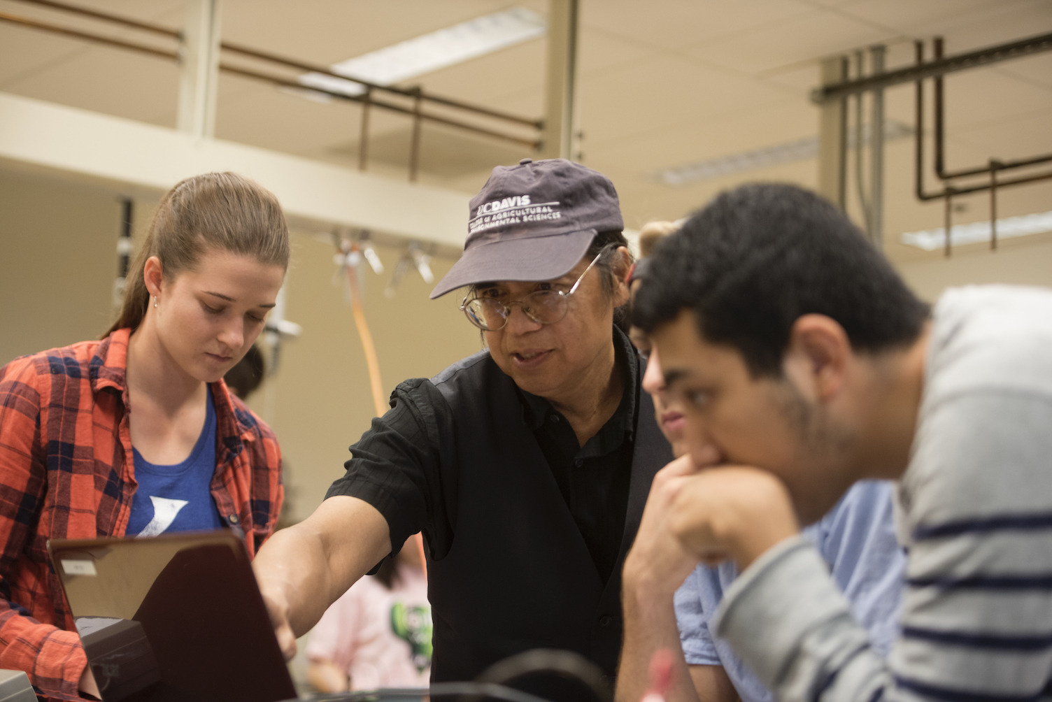 Professor surrounded by three students points out something on laptop. d a laptop