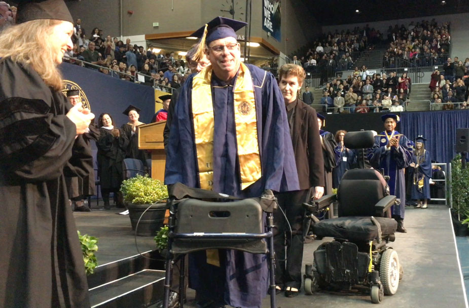 Michael O'Hearn in cap and gown, using walker.