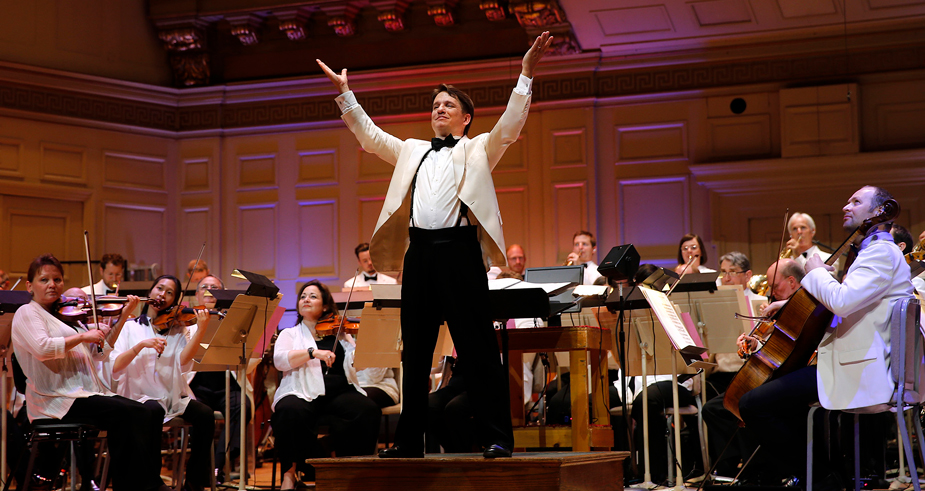 Keith Lockhart raises his arms in triumph, orchestra behind him