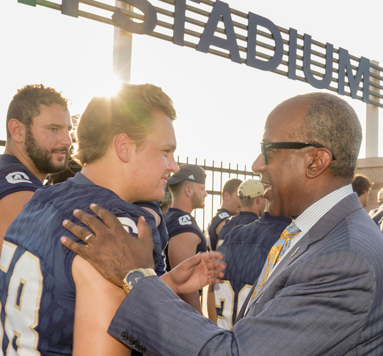 Chancellor Gary S. May greets football player, pats him on shoulder.